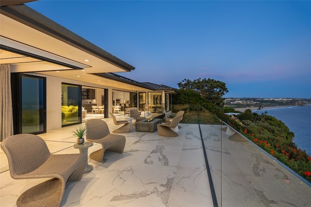 patio terrace at dusk featuring a water view and an outdoor living space