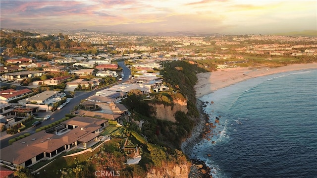 aerial view at dusk featuring a water view and a beach view