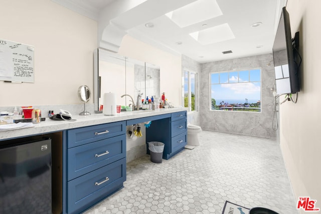 kitchen with crown molding, blue cabinets, refrigerator, and a skylight