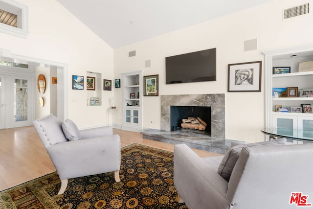 living room with built in shelves, a fireplace, hardwood / wood-style floors, and high vaulted ceiling