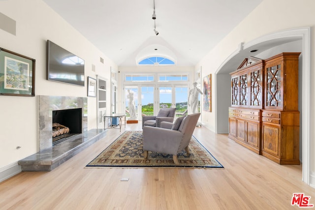 living room featuring rail lighting, a fireplace, vaulted ceiling, and light hardwood / wood-style flooring