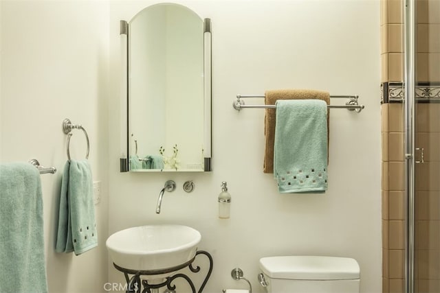 bathroom with toilet, sink, and a shower with shower door