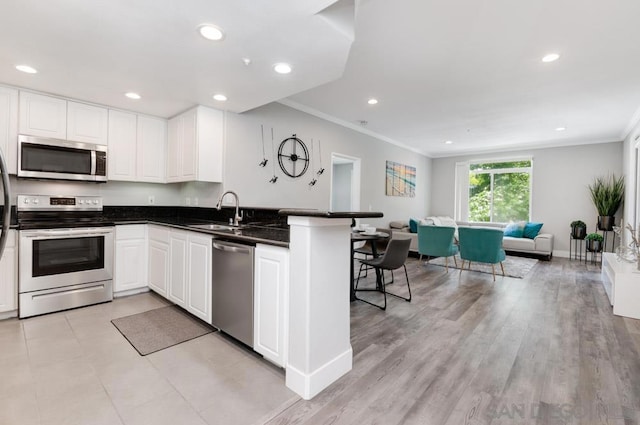 kitchen featuring white cabinets, sink, kitchen peninsula, appliances with stainless steel finishes, and crown molding