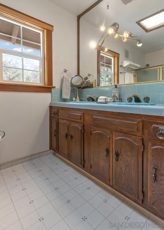 bathroom with vanity, tile patterned floors, decorative backsplash, and a skylight