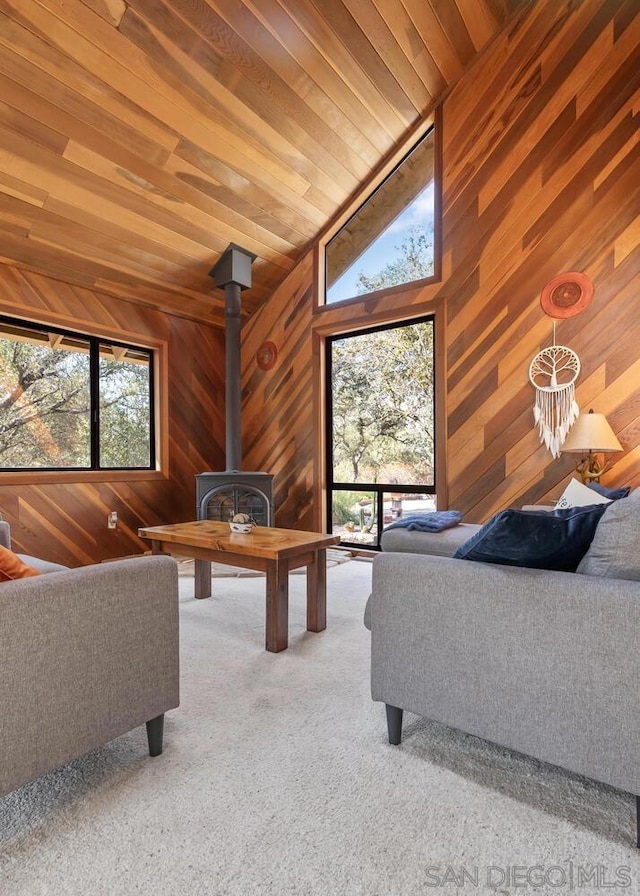 unfurnished living room featuring carpet flooring, wood ceiling, a wood stove, wooden walls, and high vaulted ceiling