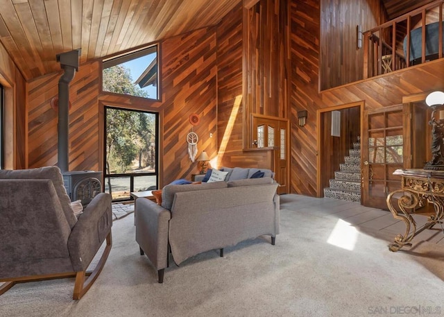 carpeted living room featuring wooden walls, high vaulted ceiling, a wood stove, and wooden ceiling