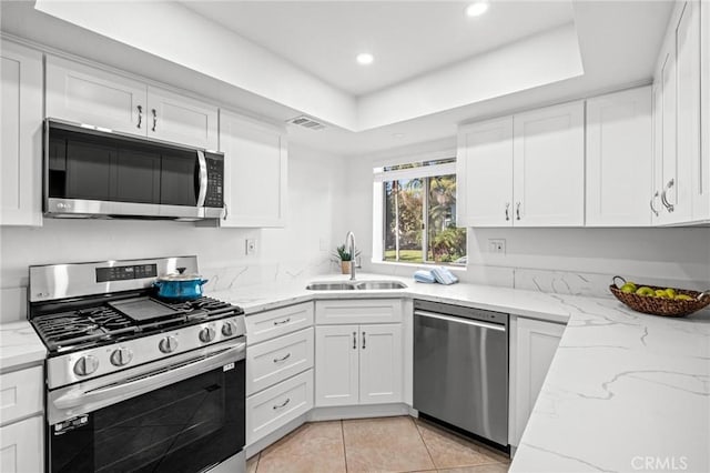 kitchen with light stone countertops, sink, light tile patterned floors, white cabinets, and appliances with stainless steel finishes