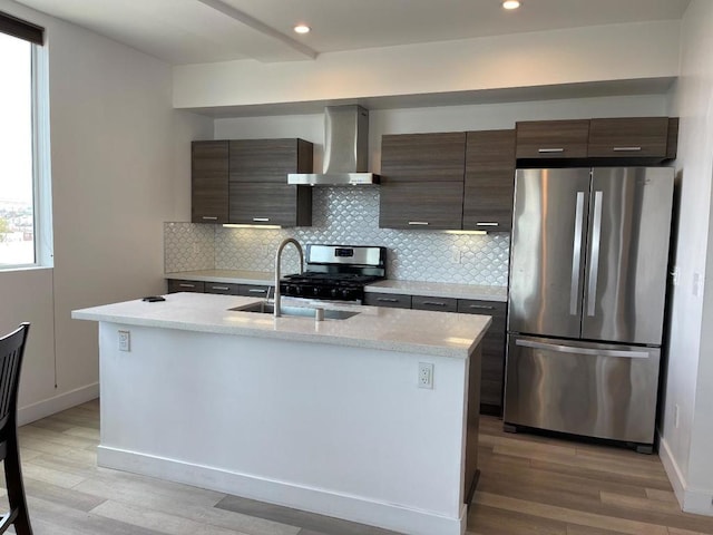 kitchen featuring stainless steel appliances, a center island with sink, dark brown cabinetry, and wall chimney exhaust hood