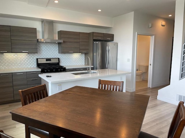 kitchen with tasteful backsplash, sink, a kitchen island with sink, stainless steel appliances, and wall chimney range hood