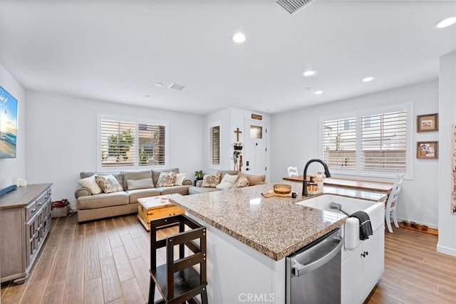 kitchen with a healthy amount of sunlight, sink, dishwasher, white cabinetry, and an island with sink