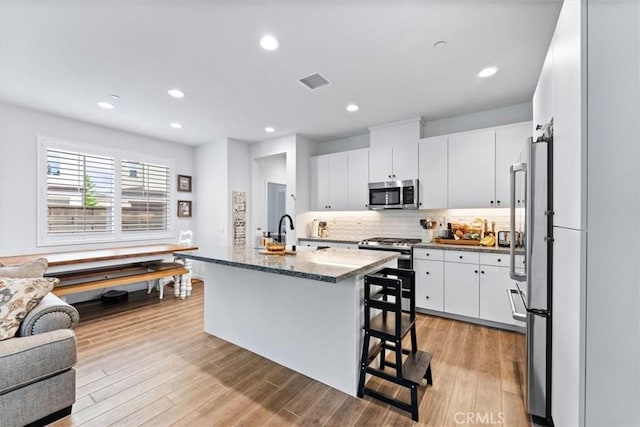 kitchen with a kitchen bar, white cabinetry, a center island with sink, and appliances with stainless steel finishes