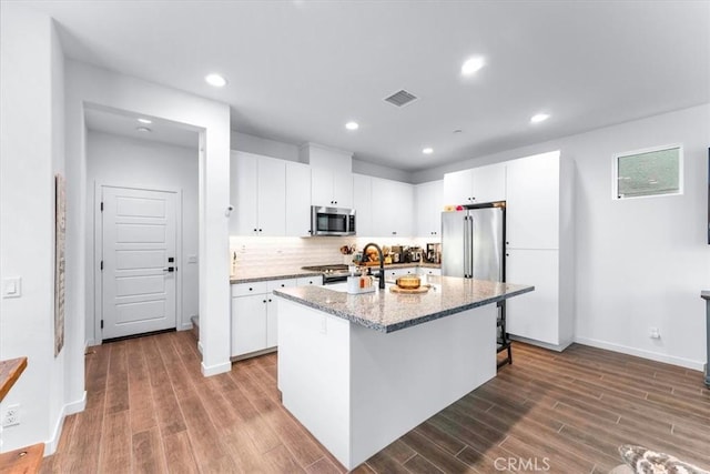 kitchen with sink, light stone counters, a center island with sink, white cabinets, and appliances with stainless steel finishes