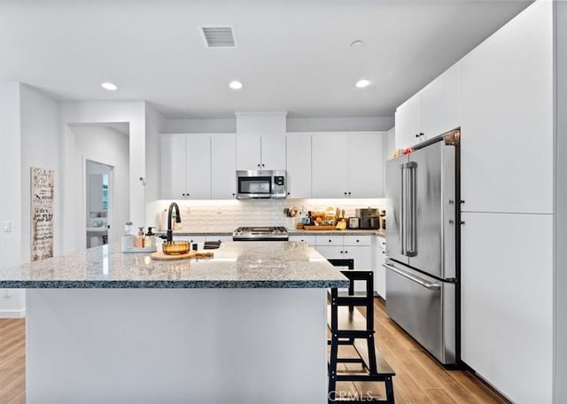 kitchen featuring tasteful backsplash, stainless steel appliances, a kitchen island with sink, sink, and white cabinets