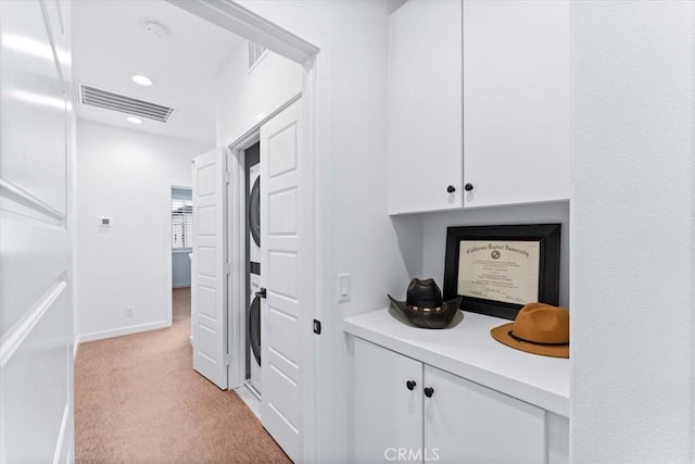 hall featuring stacked washer / drying machine and light colored carpet