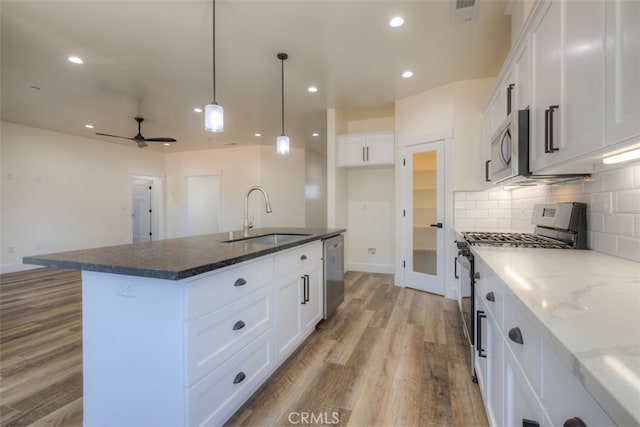 kitchen with ceiling fan, an island with sink, sink, white cabinetry, and appliances with stainless steel finishes