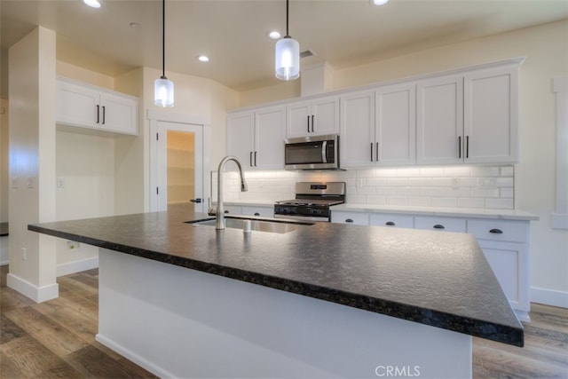 kitchen featuring white cabinets, an island with sink, hanging light fixtures, wood-type flooring, and appliances with stainless steel finishes