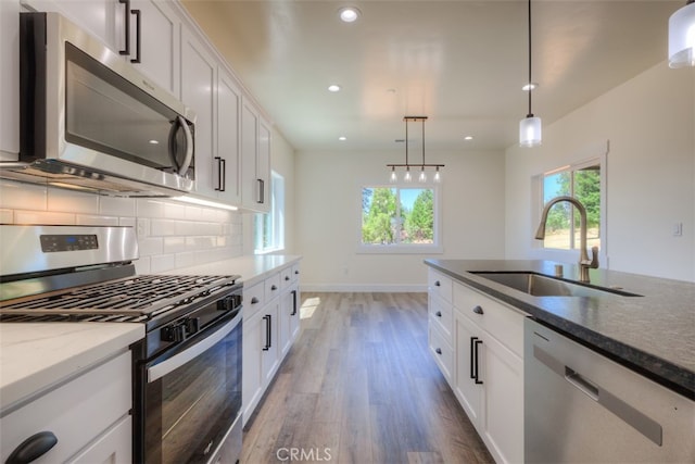 kitchen featuring wood-type flooring, sink, white cabinetry, hanging light fixtures, and stainless steel appliances