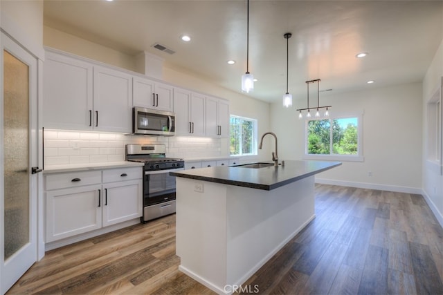 kitchen with white cabinets, an island with sink, stainless steel appliances, and dark hardwood / wood-style flooring