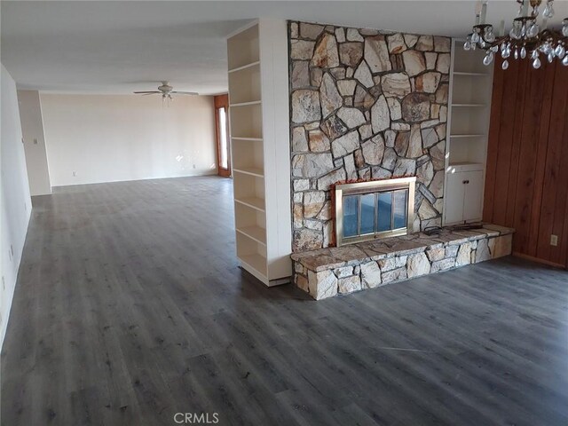 unfurnished living room with dark hardwood / wood-style flooring, a stone fireplace, ceiling fan with notable chandelier, and built in shelves