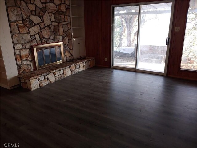 unfurnished living room featuring built in shelves, a fireplace, dark hardwood / wood-style floors, and wood walls