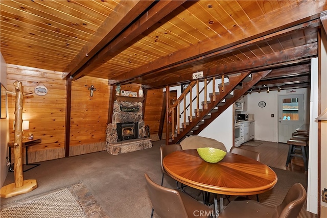 unfurnished dining area featuring wood walls, wood ceiling, a wood stove, beam ceiling, and carpet