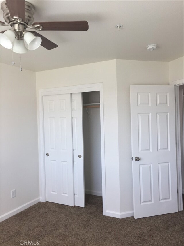 unfurnished bedroom with dark carpet, ceiling fan, and a closet