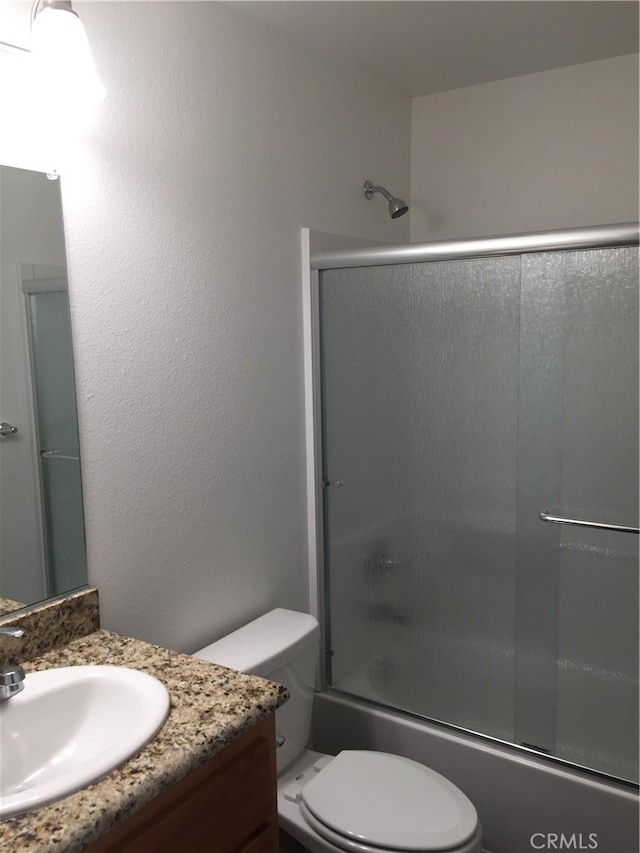 full bathroom featuring combined bath / shower with glass door, vanity, and toilet