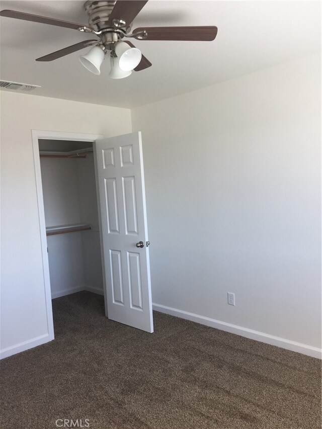 unfurnished bedroom featuring dark carpet, a closet, and ceiling fan