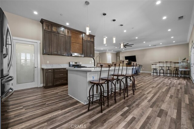 kitchen with appliances with stainless steel finishes, dark brown cabinets, hanging light fixtures, and a kitchen island with sink