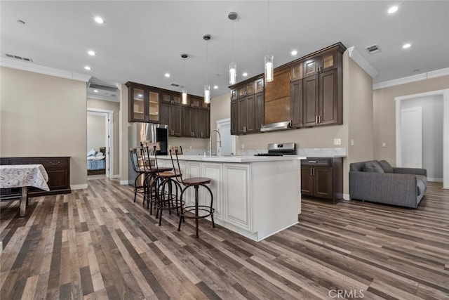 kitchen featuring hanging light fixtures, crown molding, an island with sink, appliances with stainless steel finishes, and dark hardwood / wood-style flooring