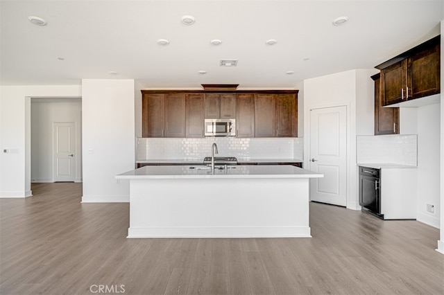 kitchen featuring sink, a center island with sink, light hardwood / wood-style floors, and dark brown cabinets