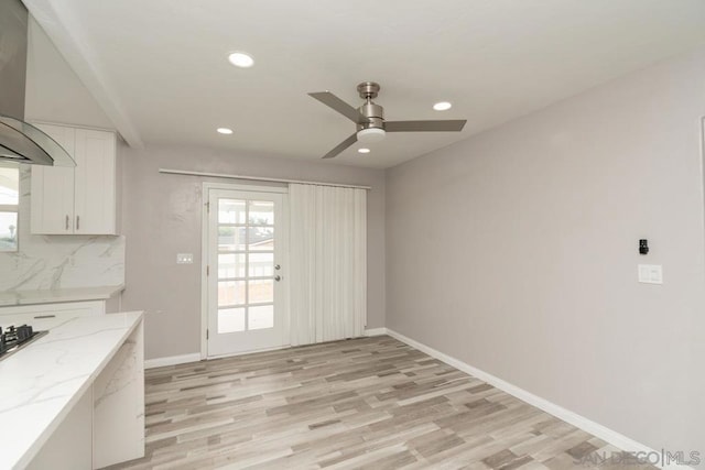 kitchen with white cabinets, light wood-type flooring, light stone counters, and wall chimney range hood