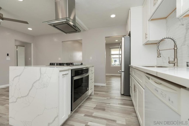 kitchen featuring island range hood, white cabinets, light stone counters, and appliances with stainless steel finishes