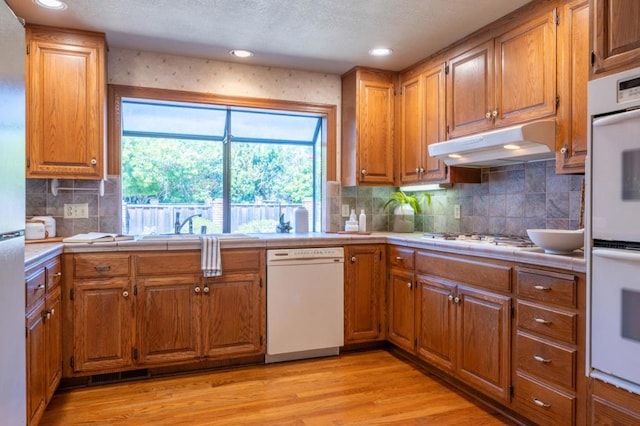 kitchen featuring tile counters, light wood-type flooring, white appliances, and tasteful backsplash