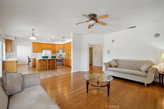 living room with ceiling fan, sink, and light wood-type flooring