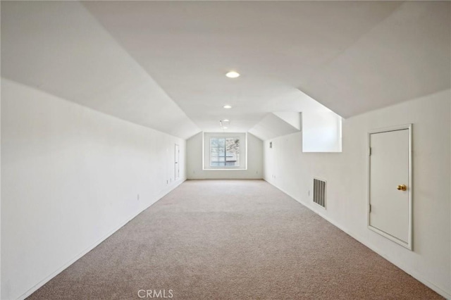 additional living space featuring vaulted ceiling and light colored carpet