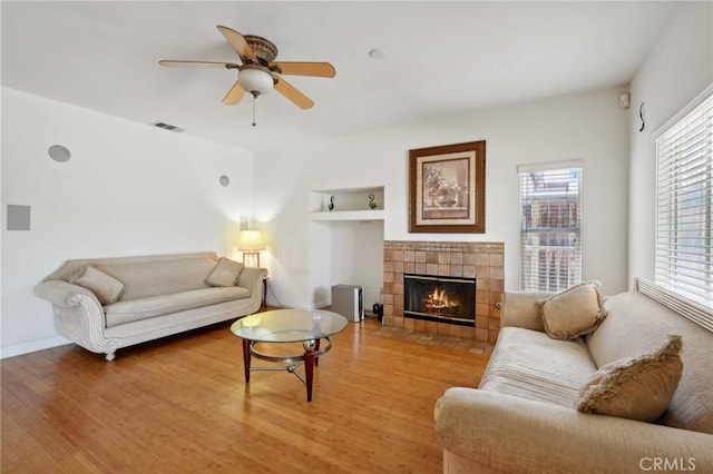 living room with hardwood / wood-style flooring, a tile fireplace, ceiling fan, and built in shelves