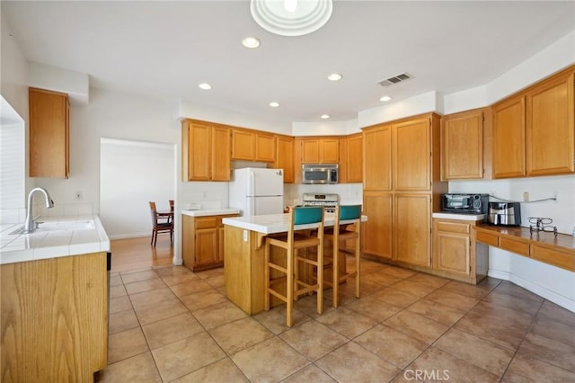 kitchen featuring sink, light tile patterned floors, appliances with stainless steel finishes, a kitchen breakfast bar, and a kitchen island