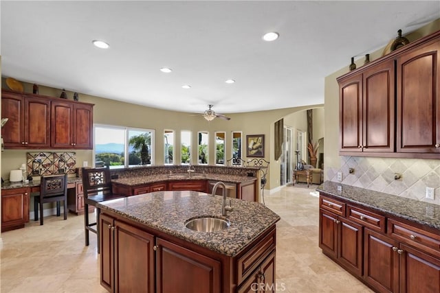 kitchen featuring arched walkways, a sink, backsplash, dark stone countertops, and a center island with sink