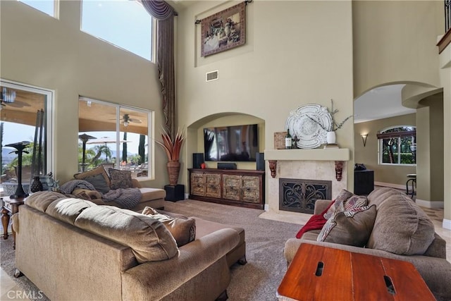 carpeted living room featuring a fireplace with flush hearth, arched walkways, visible vents, and plenty of natural light