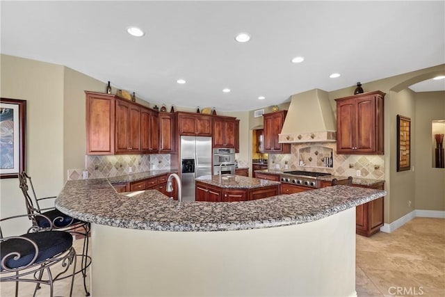 kitchen with stainless steel appliances, a breakfast bar, a peninsula, custom exhaust hood, and a center island