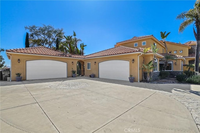 mediterranean / spanish-style home featuring concrete driveway, a tiled roof, an attached garage, and stucco siding