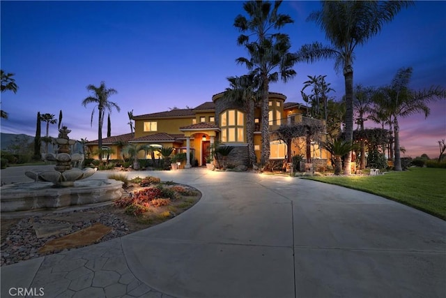 mediterranean / spanish-style house with a yard, curved driveway, a tiled roof, and stucco siding