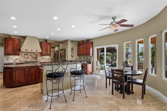 kitchen featuring a center island, a breakfast bar area, tasteful backsplash, custom range hood, and dark stone countertops