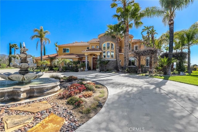 mediterranean / spanish home featuring a tile roof, driveway, and stucco siding