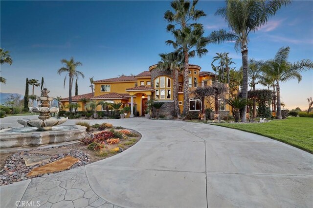 mediterranean / spanish home featuring curved driveway, a tiled roof, and stucco siding