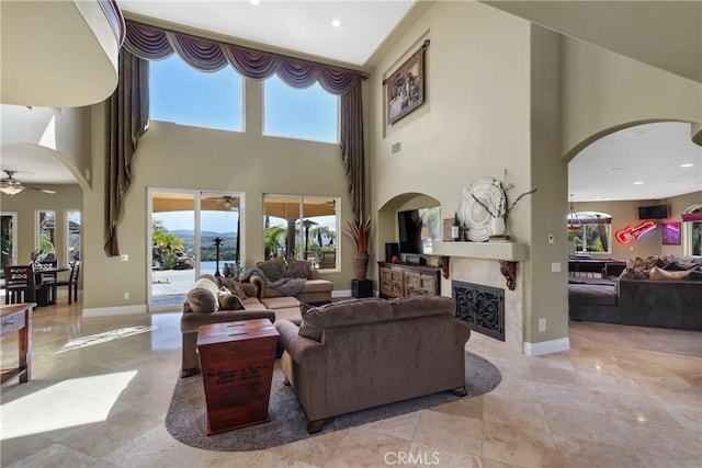 living area featuring a ceiling fan, arched walkways, a fireplace, and baseboards