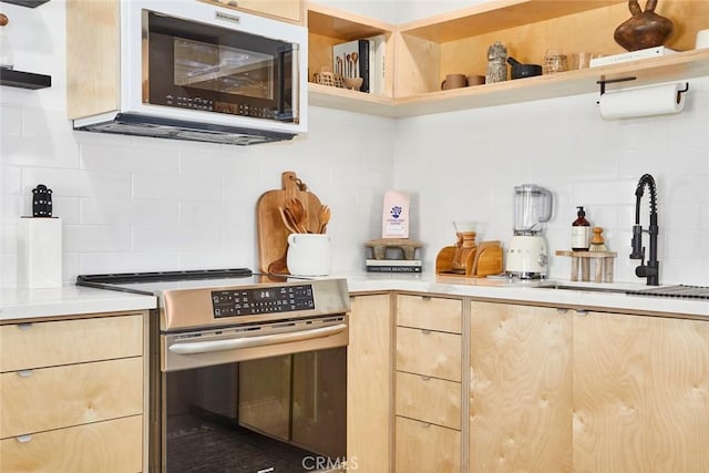 kitchen featuring tasteful backsplash, light brown cabinetry, stainless steel range, and sink