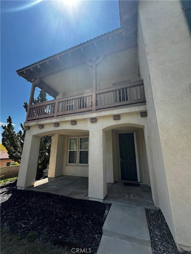 view of exterior entry featuring a balcony and a patio