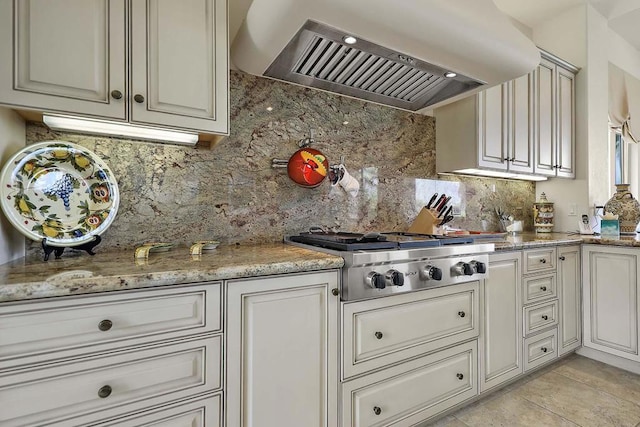 kitchen with light stone countertops, wall chimney range hood, backsplash, stainless steel gas stovetop, and light tile patterned floors